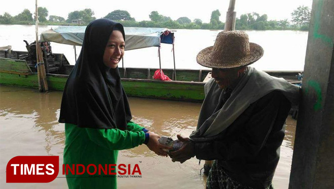 Salah satu siswi Mts Al Muniroh saat membagikan nasi bungkus ke nalayan. (FOTO: Akmal/TIMES Indonesia)