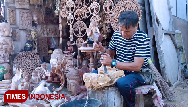 Ragum saat memahat kayu di depan Art Shopnya. Bertempat di Pantai Mertasari Denpasar Selatan. Kamis (23/8/2018). (FOTO: Khadafi/TIMES Indonesia)
