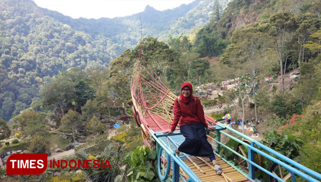 Pengunjung wisata Watu Rumpuk berfoto di rumah perahu yang memiliki latar belakang pegunungan.