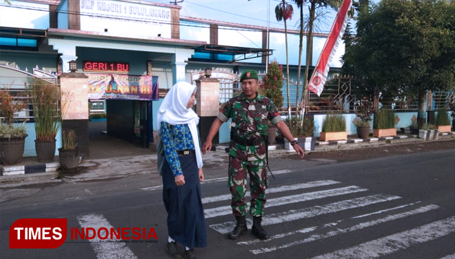 Koptu Yatno menyeberangkan siswa SMP 1 Bululawang. (FOTO: AJP/TIMES Indonesia)