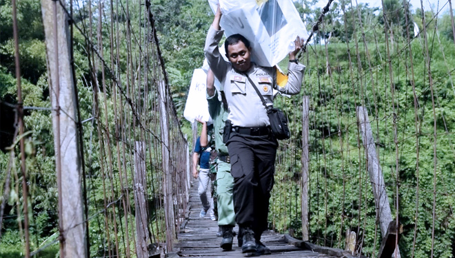 Bripka Suryadi saat melewati jembatan gantung dengan konstruksi seadanya, untuk mendistribusikan logistik ke TPS terpecil di tempat ia bertugas (FOTO: Istimewa) 