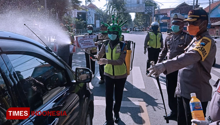 Polres Pamekasan gunakan helm corona semprotkan disinfektan pada mobil di jalan raya Jokotole Pameksan.(Foto: Akhmad Syafi'i/TIMES Indonesia)