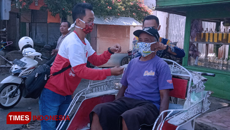 Tampak pemilik sanggar Ijen Batik Tamanan Bondowoso memberikan dan memasangkan masker batik ke sejumlah abang becak di Pasar Tamanan (FOTO: Moh Bahri/TIMES Indonesia).