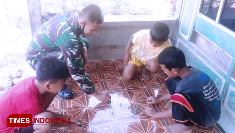 Anggota Satgas sedang Bermain Kelereng dengan Anak-Anak. (FOTO: AJP/TIMES Indonesia)