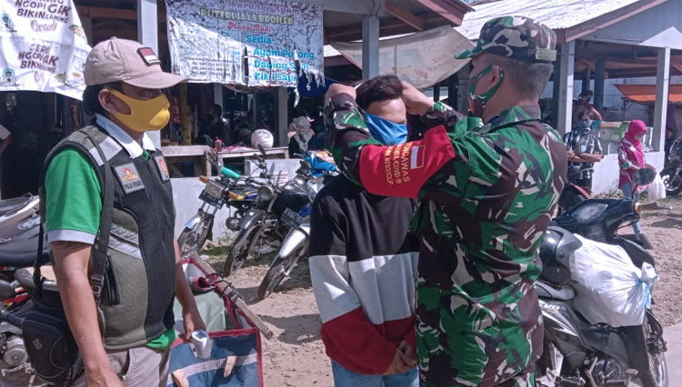 Anggota Koramil 16 Wanareja, memakaikan masker kepada seorang warga di pasar Bantar Wanareja. (Foto: pendim Cilacap for TIMES Indonesia)
