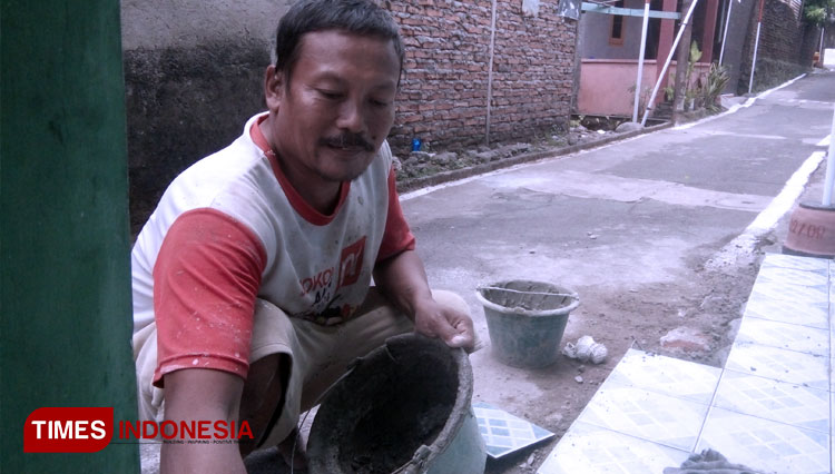 Sutino sedang bekerja merenovasi halaman sebuah rumah. Di saat pandemi covid-19 ini penghasilannya tidak menentu, namun dirinya tetap bersikukuh tidak mengambil honornya agar tidak membebani warga. (FOTO: Mushonifin/TIMES Indoensia)