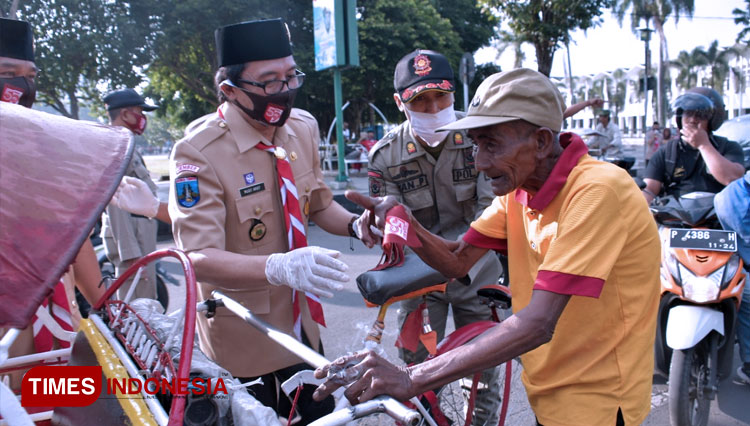 Ketua Kwarcab Pramuka Jember KH Abdul Muqit Arief membagikan masker kepada salah satu tukang becak di kawasan Alun-Alun Jember, Jumat (14/8/2020). (FOTO: Dody Bayu Prasetyo/TIMES Indonesia)