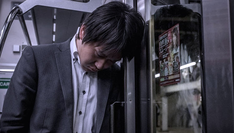 Seorang pria Jepang tertidur di kereta yang membawanya pulang ke rumah setelah seharian bekerja. Hal biasa bagi para pekerja di Jepang menumpang kereta terakhir ke rumah setiap malam.(FOTO: BBC/Getty Image)
