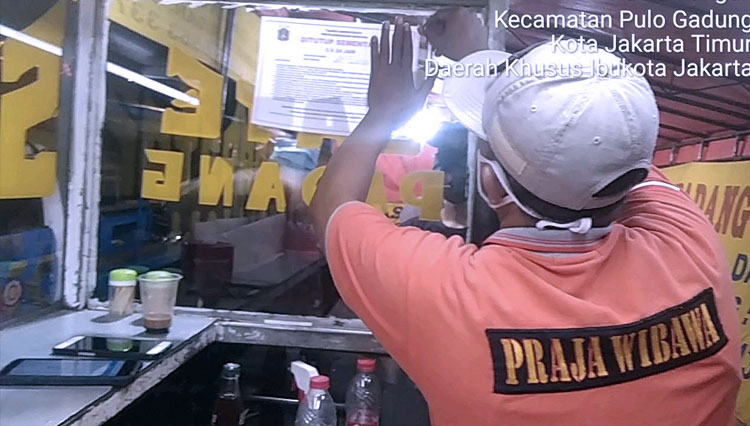 Anggota Satpol PP Kelurahan Rawamangun yang tengah menempelkan penyegelan sementara tempat usaha yang tidak menanggapi himbauan Satpol PP. (Foto: Kominfotik Jakarta Timur)