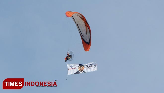 Pilot paramotor menerbangkan parasut dan membawakan poster di acara Penutupan Pesmaba UMM. (Foto: Naufal Ardiansyah/TIMES Indonesia)