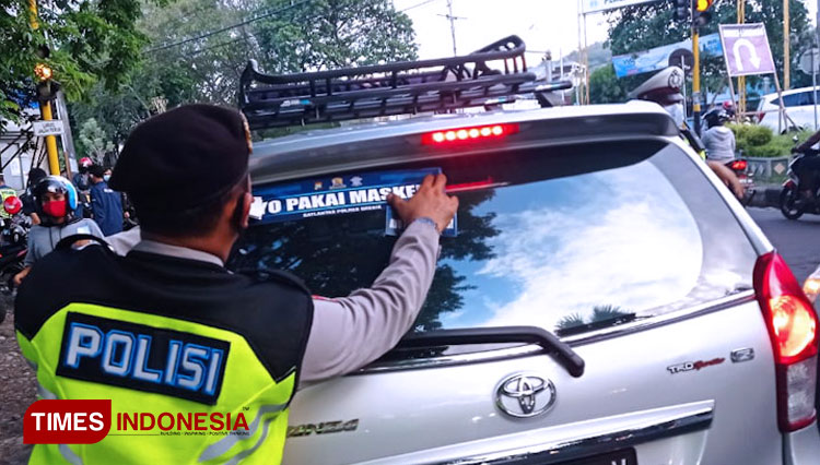 Polisi saat menempel stiker di kendaraan roda empat sebagai bentuk kampanye penerapan 3M (Foto: Akmal/TIMES Indonesia)