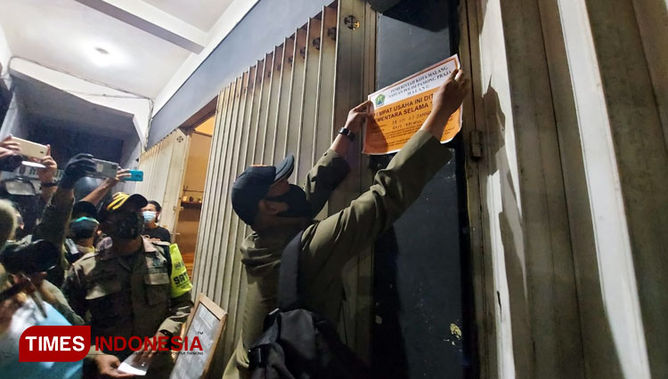Salah satu petugas Satpol PP saat menempelkan segel penutupan sementara selama 14 hari kepada salah satu kafe di Kota Malang saat melakukan operasi PPKM, Jumat (15/01/2021). (Foto: Rizky Kurniawan Pratama/TIMES Indonesia)
