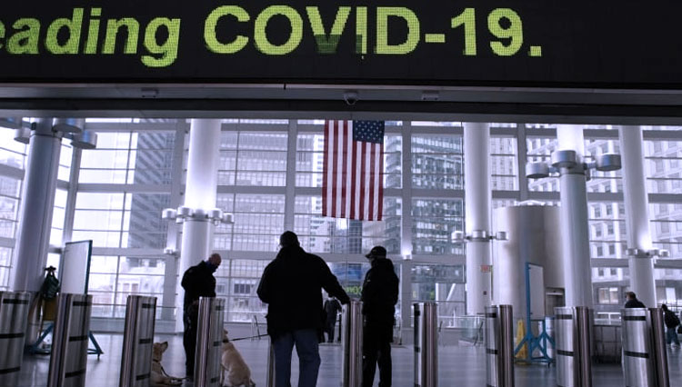 Informasi Covid-19 ditampilkan di layar saat orang-orang berjalan di sekitar Stasiun Feri Selatan di New York, pada 5 Januari. (FOTO: Al Jazeera/Reuters)