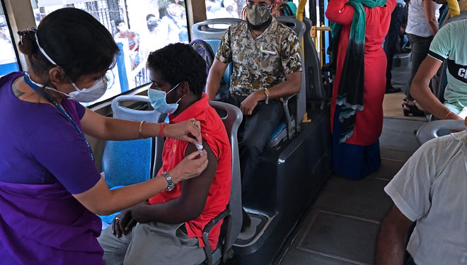 Seorang petugas kesehatan memvaksinasi seorang pria dengan vaksin Covishield terhadap Covid-19 di bus penumpang (FOTO: Global Times/AFP)