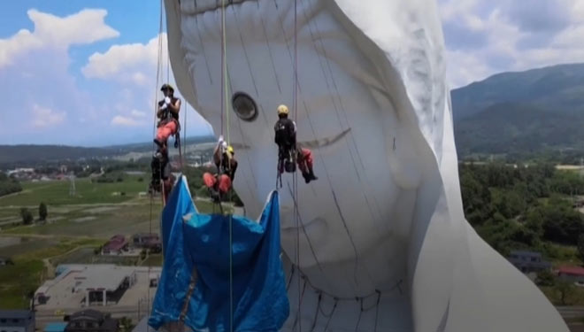 Para pekerja saat memasangi masker pada wajah patung raksas Dewi Belas Kasihan, Kannon, di kuil Houkokuji Aizu Betsuin di Prefektur Fukushima, Jepang.(FOTO : BBC)