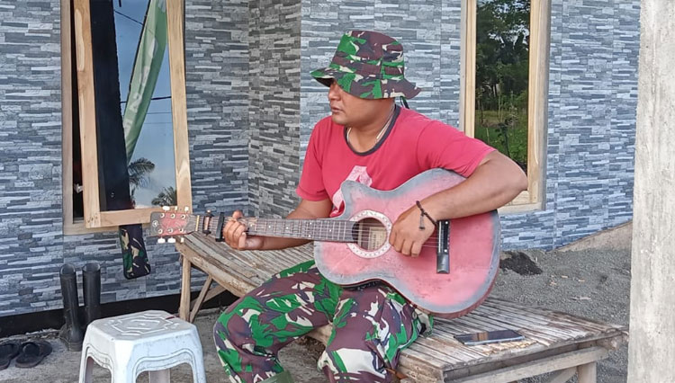 Praka Dedimus terlihat menikmati bermain gitar usai bekerja seharian (Foto: Riswan Efendi/TIMESIndonesia)