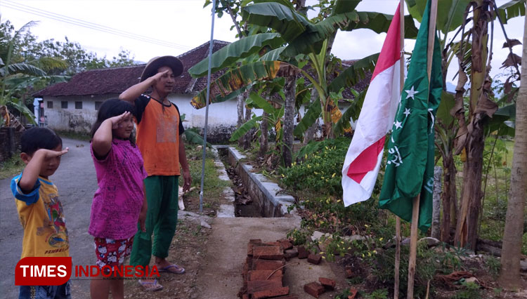 Edi Susanto lakukan penghormatan kepada benderah merah putih dan bendera NU didepan Rumahnya didampingi dua anak kecil di sebelah kanannya (FOTO: Yusuf For TIMES Indonesia)
