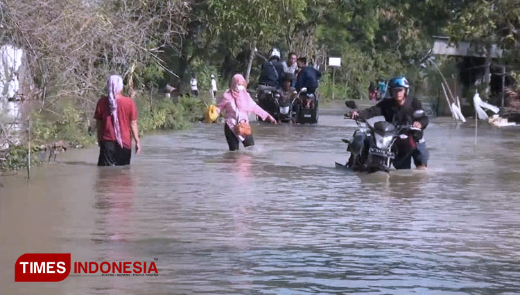 Pengendara sepeda motor terpaksa mendorong kendaraannya yang mogok, saat mencoba menerobos jalan yang tergenang air akibat banjir luapan Bengawan Jero. (FOTO: MFA Rohmatillah/TIMES Indonesia)