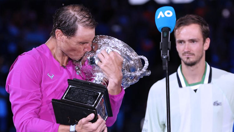 Rafael Nadal (kiri) disaksikan petenis Daniil Medvedev dengan emosial mencium piala turnamen Australia Terbuka setelah ia menang dengan perjuangan yang melelahkan 2-6 6-7 (5-7) 6-4 6-4 7-5 di Rod Laver Arena. (FOTO: BBC)